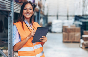 A woman in high vis uses her tablet to check on her supply chain management while in the warehouse