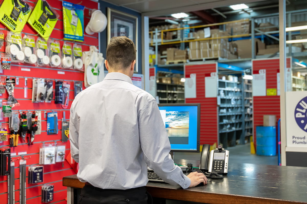 A shot from behind of a Galvins employee using their compyter at the sales counter with the warehouse in the background