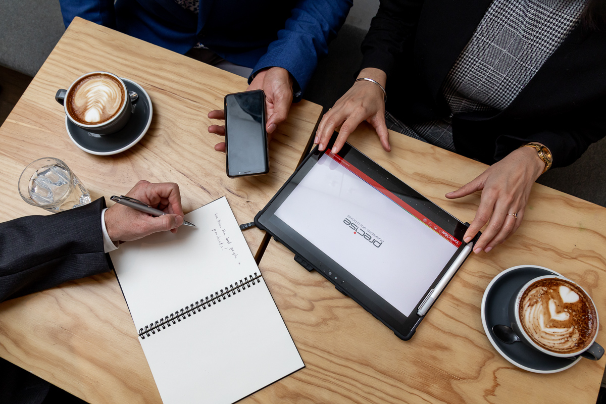 Precise workers meeting in a coffee shop with both technology and old school notetaking