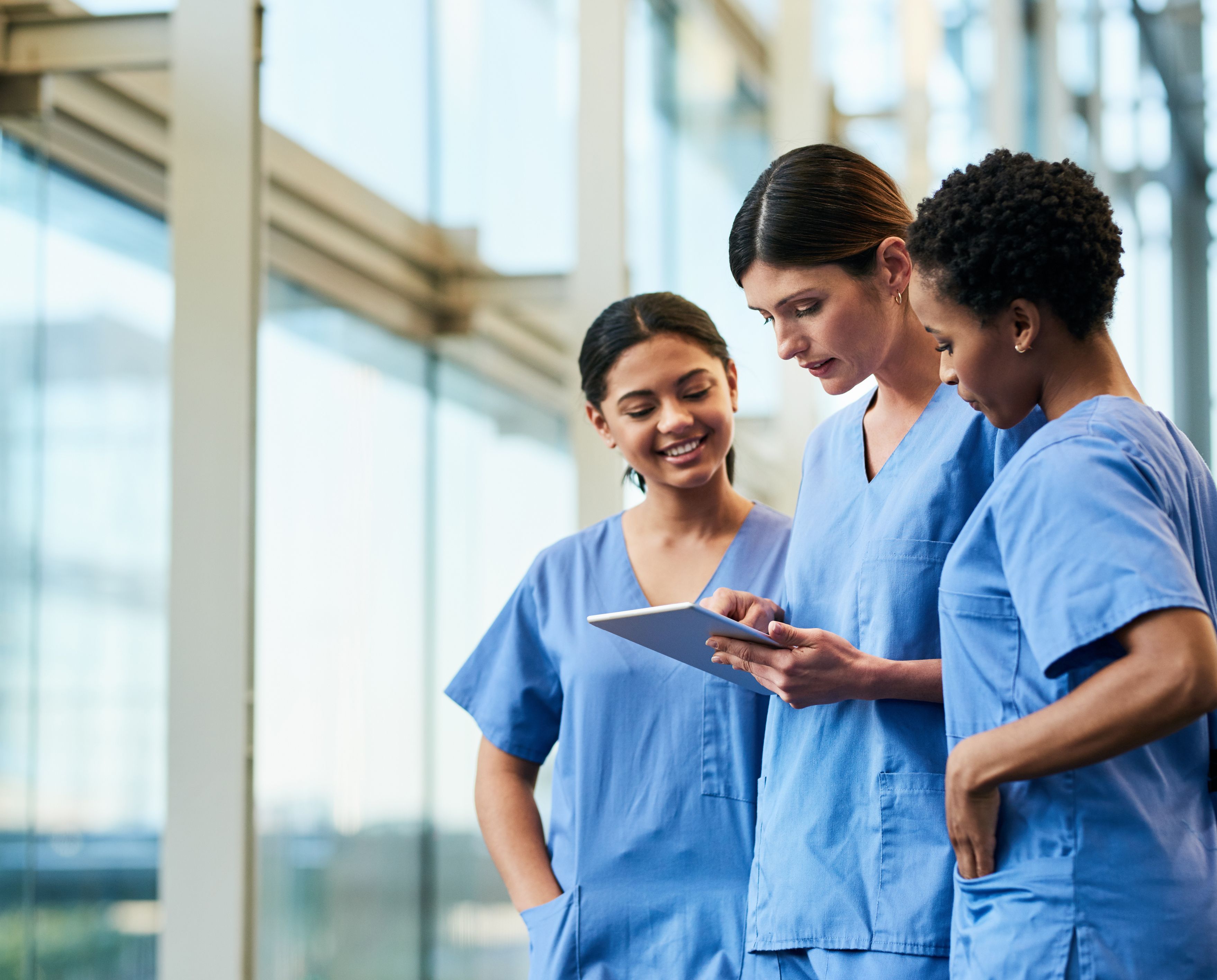 Three carers in scrubs standing together looking at tablet