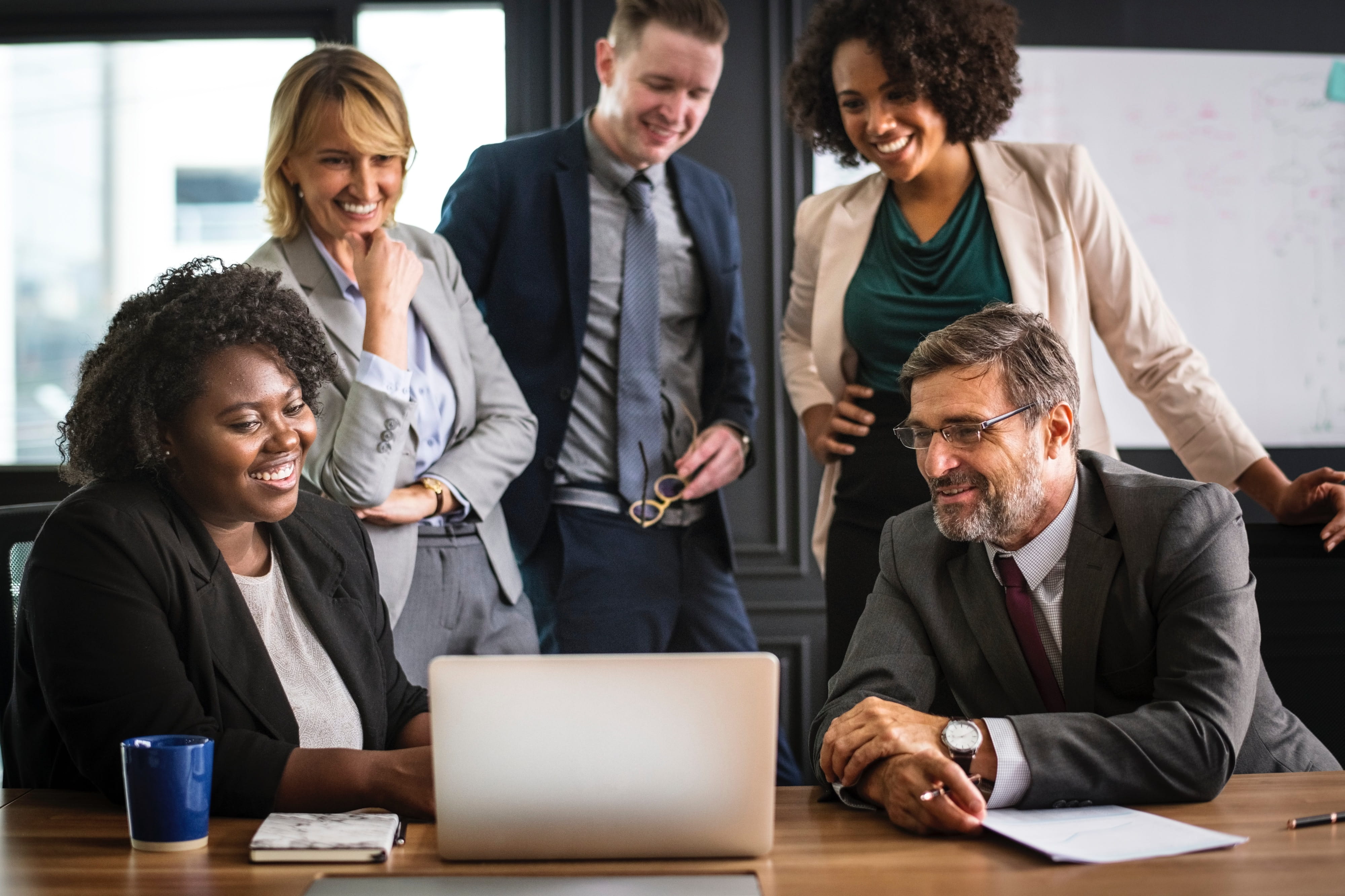 A group of people in office attire gathered around a laptop looking at something on the screen