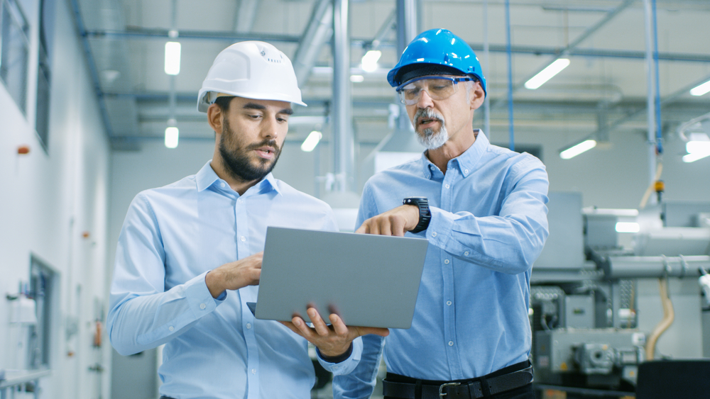 Two men in a mondern factory discussing what is on the laptop screen